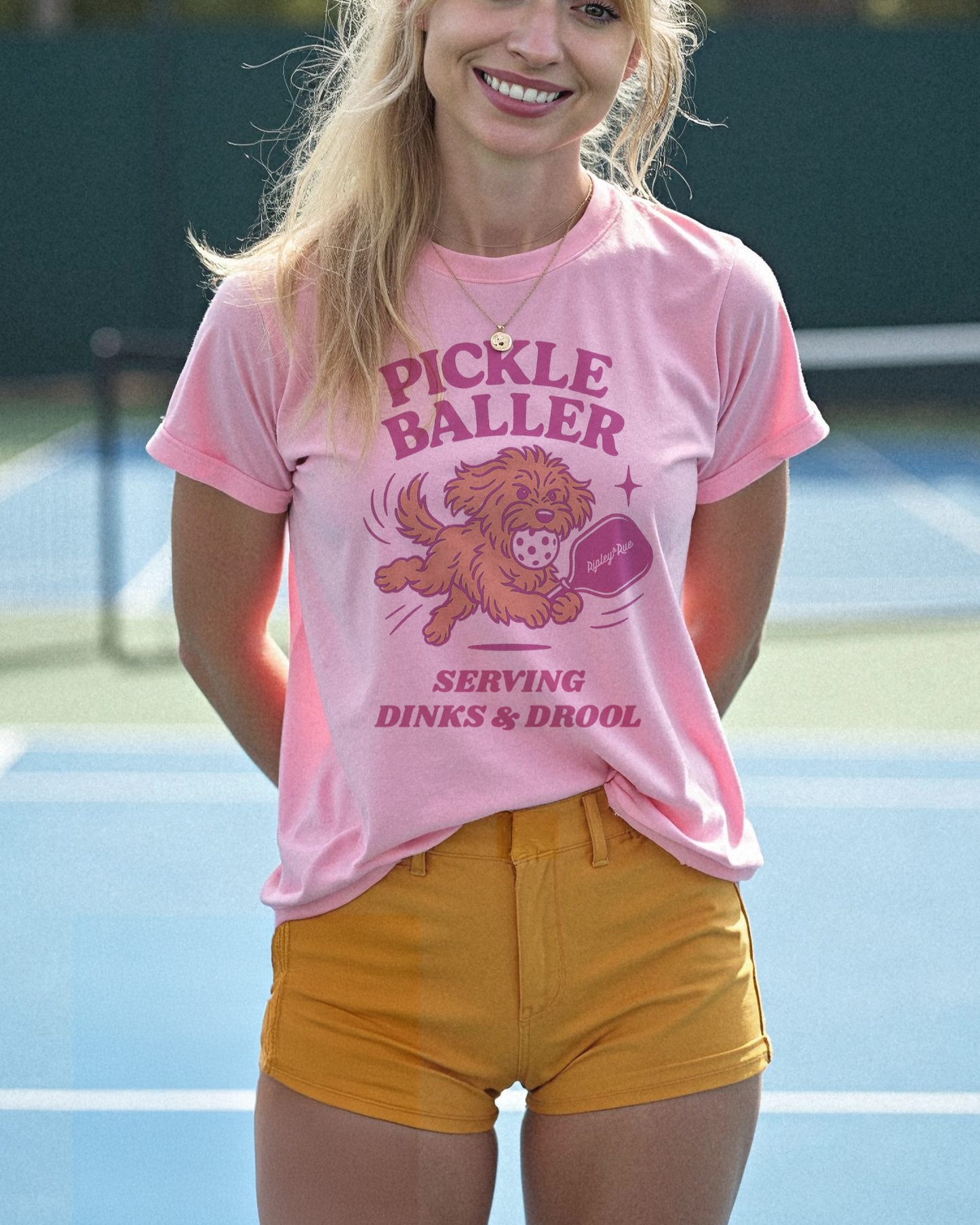 Person wearing a pink 'Pickle Baller' t-shirt on a tennis court